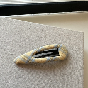 Detailed view of yellow and blue plaid fabric hair clip on a beige woven texture surface