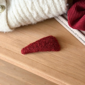 Close-up of a plush burgundy heart hair clip on a warm winter knit background