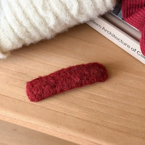 Detail of a deep red plush heart-shaped hair clip on a cozy winter knit background