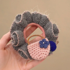 Detail of grey plush scrunchie with pink hand-knitted bag charm and blue flower detail