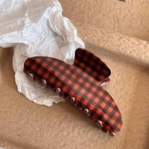 Detailed view of cocoa brown checkered hair claw clip on neutral textured paper background