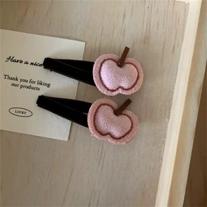 Dettaglio di un paio di fermagli per capelli a mela rosa floccati su fondo in legno chiaro