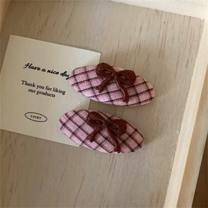 Dettaglio di fermagli in tessuto a quadretti rosa e neri con fiocchi ricamati marroni