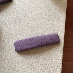 Detail of purple plaid fabric hair clip showing textile texture on a cream background