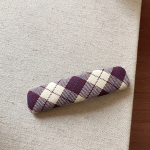 Detail view of a purple argyle fabric hair clip with classic check pattern on linen