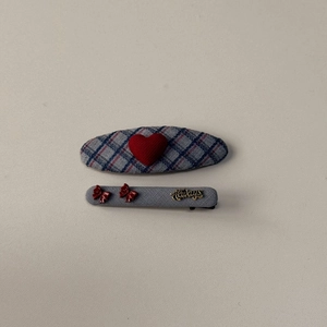 Detailed view of grey plaid fabric hair clips set with red hearts and Always lettering