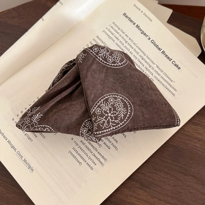 Close-up of a dark coffee brown paisley fabric hair clip on a vintage open book