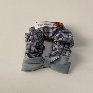 Detail of blue-grey plaid fabric scrunchie with wooden button and Rise Above label