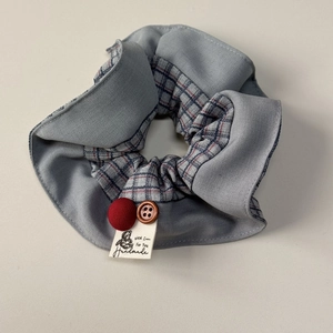 Detailed view of blue-red plaid scrunchie with a handmade label and button decor