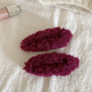 Detail view showing a pair of plush oval hair clips in dark magenta wool fabric texture