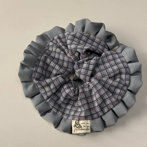 Detailed close-up of blue-grey plaid fabric scrunchie with handmade cotton woven label