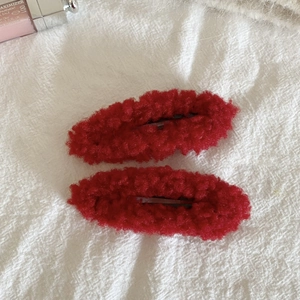 Detail shot of two red plush fleece snap hair clips on white fabric background