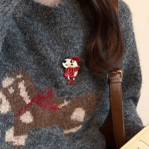 Close-up of embroidered puppy brooch with red hat on a cozy mohair sweater
