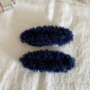 Detail showing a pair of navy blue plush fleece hair clips on a white fabric background