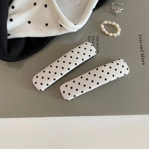 Detail view of two fabric-covered polka dot hair clips with black spots on white base
