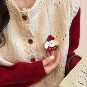 Close-up of a handmade cute puppy brooch with red beret pinned on a beige knitted sweater