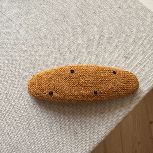 Detailed view of handmade knitted oval hair clip with yellow fabric and black polka dots
