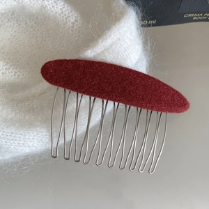 Close-up of red velvet hair comb with silver metal teeth on a white soft plush background