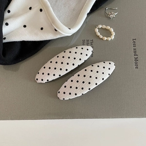 Detail shot of two minimalist beige polka dot hair clips on a textured display board