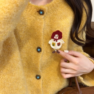 Detail of cute embroidered bird brooch with red hood on yellow textured cardigan
