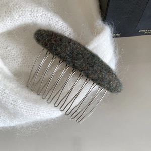 Detail view of dark green felt hair comb with silver metal teeth on soft knit fabric