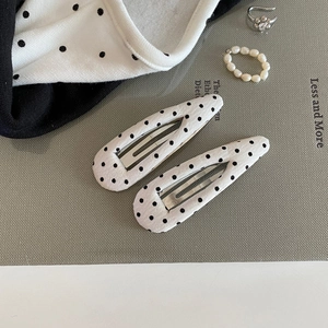 Close-up of white fabric hair clips with black polka dots on a textured background