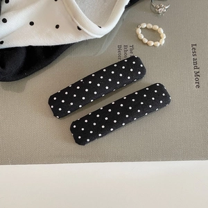 Close-up of elegant black fabric hair clips with white polka dots and pearl accessories