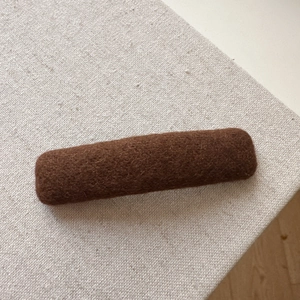 Close-up of a handmade brown knitted hair clip on a soft textured fabric background