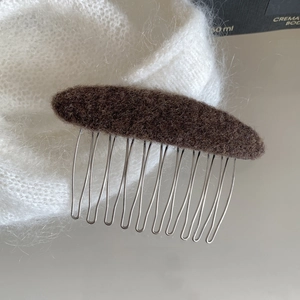 Detailed close-up of a brown wool felt hair comb with silver metal teeth on knit fabric