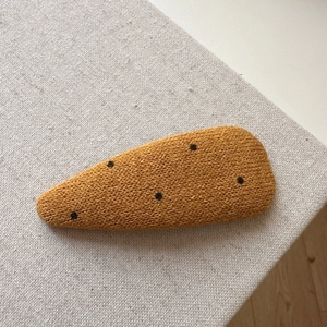 Detailed view of ginger yellow knitted polka dot hair clip on beige textured fabric