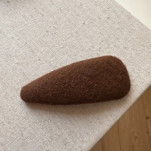 Close-up of a warm brown wool felt hair clip showing rich handmade fiber texture