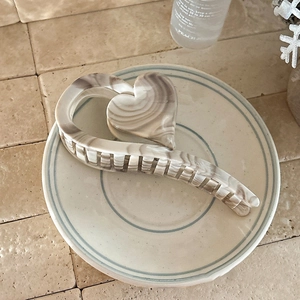 Detailed close-up of cream heart hair claw clip with marble texture on ceramic plate