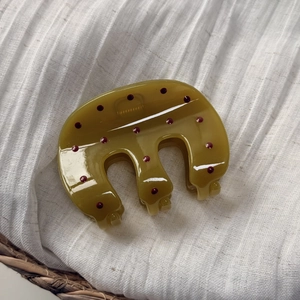 Détail de la pince à cheveux vert olive à pois rouges sur un tissu en lin blanc