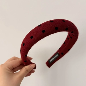 Detailed close-up of dark red polka dot headband featuring a handmade inner label