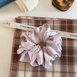 Detail view of large lavender satin scrunchie with soft folds on a plaid fabric background