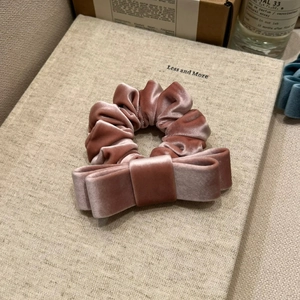 Close-up of luxury dusty rose velvet bow scrunchie on a minimalist beige background