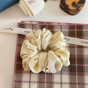 Detail of a cream satin scrunchie with silky folds and elegant pearl luster finish