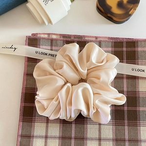 Detailed close-up of cream satin scrunchie with soft silk texture on checkered cloth