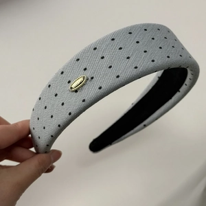 Dettaglio ravvicinato della fascia per capelli spessa grigio chiaro a pois con logo oro