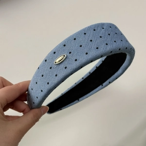 Dettaglio del cerchietto azzurro a pois in tessuto di lino testurizzato con logo in metallo