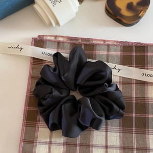 Detailed close-up of a large black matte satin scrunchie with ruffled edges on a fabric mat