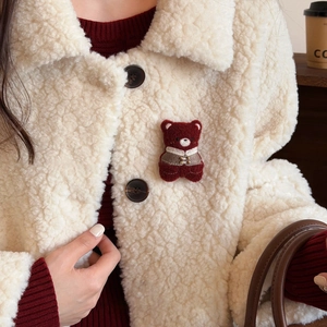 Detail of red plush bear brooch with traditional vest on cream fleece jacket