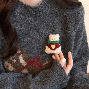 Cute teddy bear brooch wearing a red heart sweater and green scarf on a wool coat