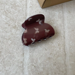 Close-up of a burgundy butterfly hair claw clip with floral patterns on a marble surface