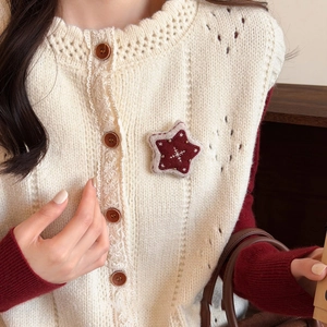 Detail of star-shaped embroidery brooch on beige openwork knit vest and red sweater