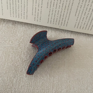 Close-up of denim blue hair claw clip with red polka dots on textured beige background