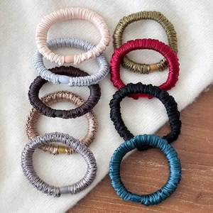 Detail of nine multi-colored satin hair ties on a white sweater and wooden table