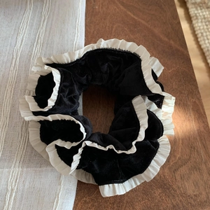 Dettaglio di scrunchie in velluto nero con bordo bianco a volant su un tavolo