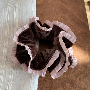 Dettaglio di scrunchie in velluto marrone con bordo plissettato rosa su legno rustico