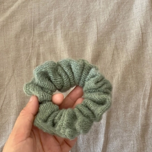 Hand holding a grey-green knitted scrunchie showing elastic texture on fabric background